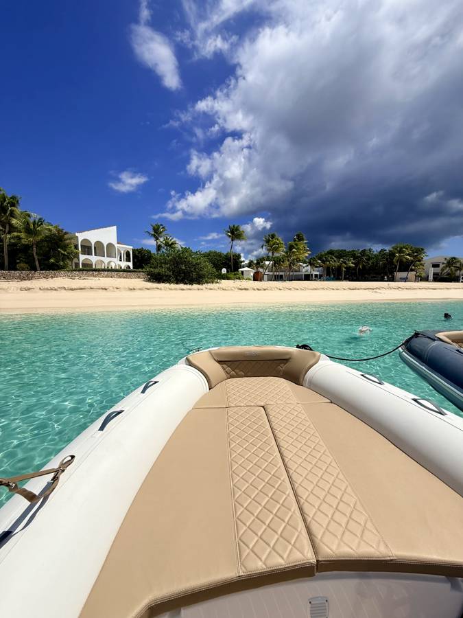 The RIB's bow sun pad, anchored off a white-sand beach lined with palms, Saint-Martin